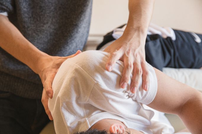 Person in weißem T-Shirt erhält eine Rückenmassage von einer anderen Person in grauem Shirt