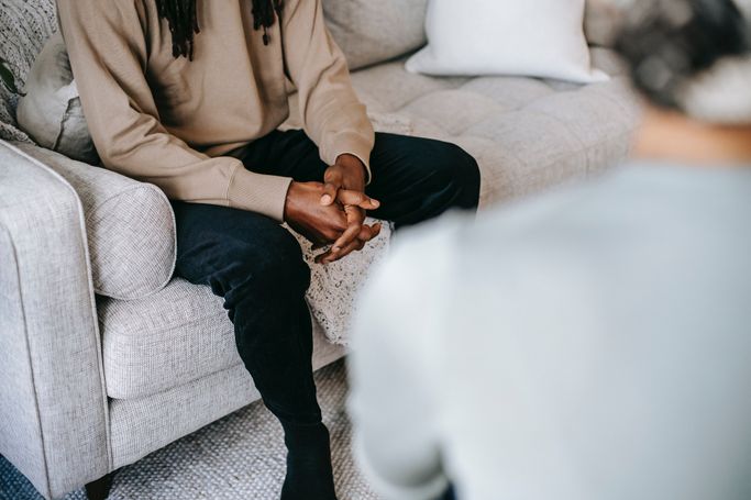 Person sitzt mit verschränkten Händen auf einem Sofa, Gesprächspartner unscharf im Vordergrund